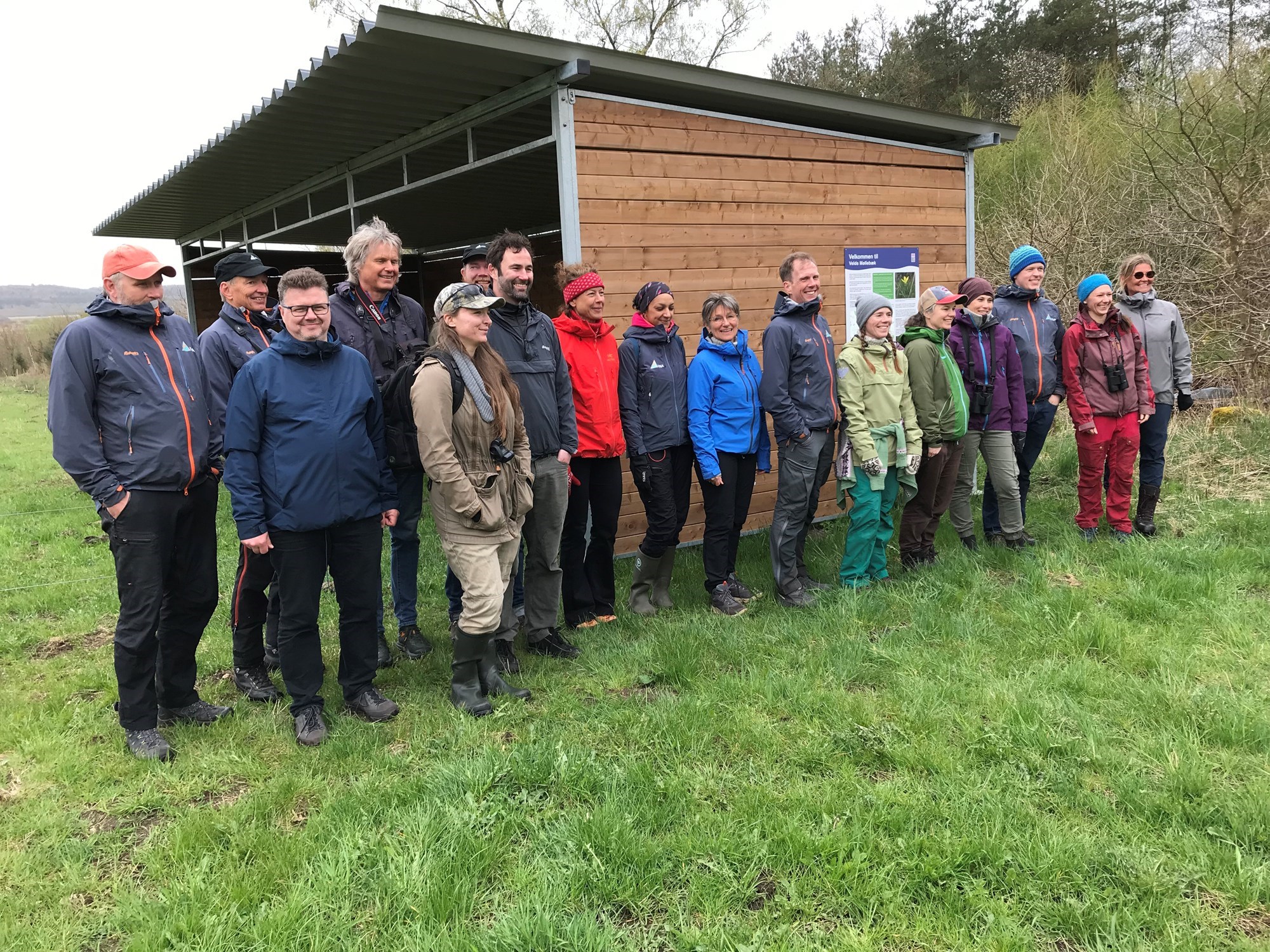 En gruppe voksne ved et skur på en mark