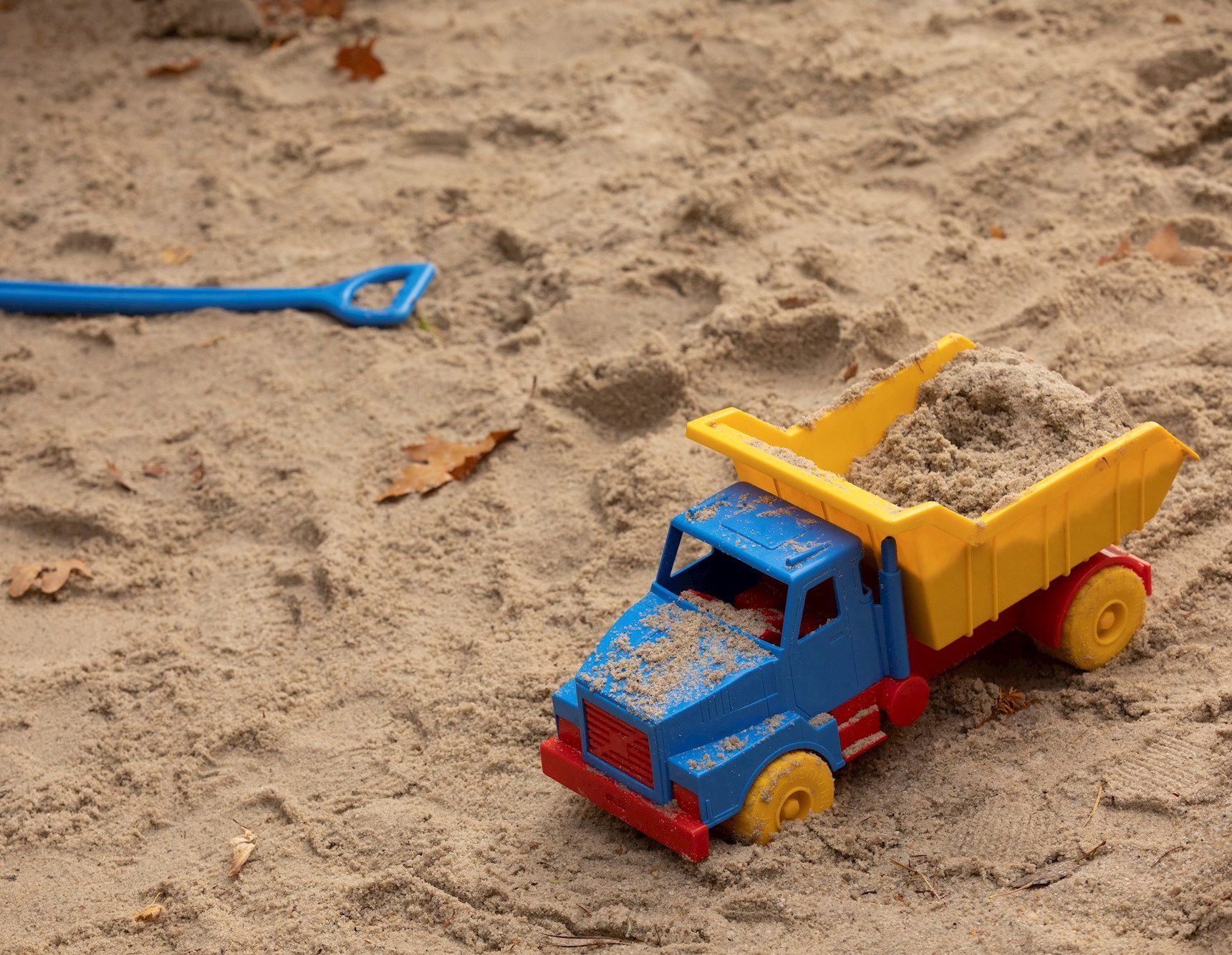 Legetøjslastbil og skovl, der ligger i sandkasse